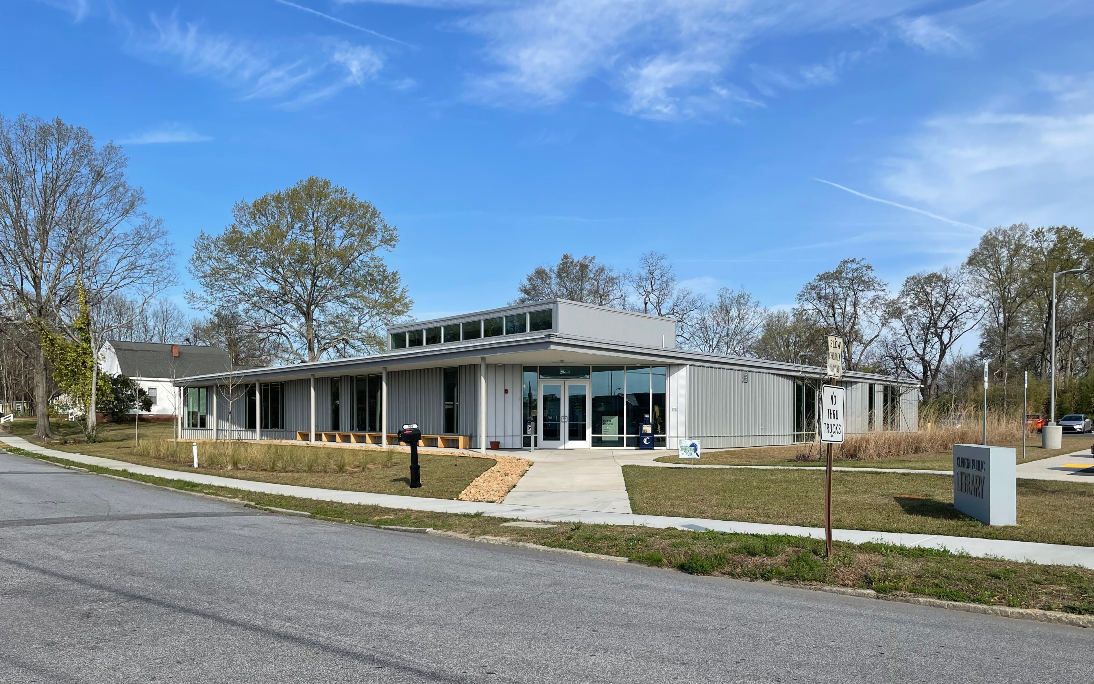Exterior view of a modern public library building with a gray metal façade, large windows, and a front entrance, set against a clear blue sky.